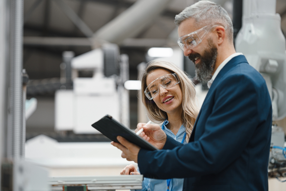 Femaleengineerandmaleproductionmanagerstandinginmodernindustrial | itvibes Female Engineer and Male Production Manager Standing in Modern Industrial Factory Talking About Production Manufacturing Facility with Robotics and Automation